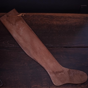 May include: A wooden sock form, a tool used for stretching and shaping socks, is shown on a dark brown wooden surface.