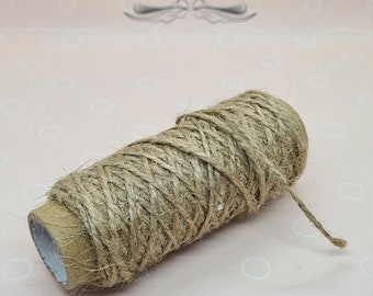 May include: A roll of natural jute twine. The twine is wrapped around a cardboard tube. The background is a light pink surface with the text "LuuceCreates Quarantine Dreams".