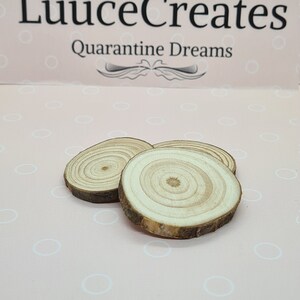 May include: Three small, round wooden slices with visible growth rings and bark edges. The slices are arranged on a pink surface with a pattern of white circles. The text "LuuuceCreates Quarantine Dreams" is visible in the background.