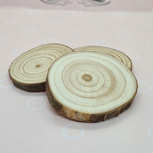 May include: Three small, round wooden slices with visible growth rings and bark edges. The slices are light brown and tan, arranged on a pink background with the text "luuceCreate Quarantine Dreams" at the top.