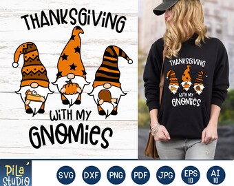 May include: Thanksgiving with my gnomes graphic design featuring three gnomes holding a pumpkin, a pie, and a turkey leg. The gnomes are wearing orange, brown, and black striped hats. The text "Thanksgiving with my gnomes" is written in black.