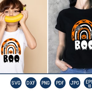 Puede incluir: Dos camisetas, una blanca y otra negra, con un dise&ntilde;o de arco&iacute;ris de Halloween. El arco&iacute;ris presenta murci&eacute;lagos naranjas, telara&ntilde;as y una calabaza. La palabra "BOO" est&aacute; escrita en blanco con efectos de goteo.