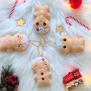 Pode incluir: Enfeites de Natal com bonecos de gengibre sorridentes, bengalas doces e estrelas decorativas. Os enfeites estão dispostos sobre uma superfície branca e fofa com luzes de corda e um enfeite de trem vermelho.