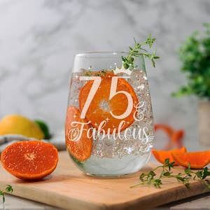 May include: A clear glass with the text "75 & Fabulous" etched on the side. The glass is filled with water and orange slices.