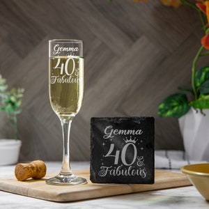 May include: A personalised champagne flute and slate coaster with the text "Gemma 40 & Fabulous" engraved in white. The flute is filled with champagne and the coaster is black.