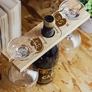 Könnte beinhalten: Holz-Wein- und Glashalter mit zwei herzförmigen Ausschnitten. Die Herzen sind mit dem Text "35. Jahrestag" und "Unser 35. Jahrestag" graviert.
