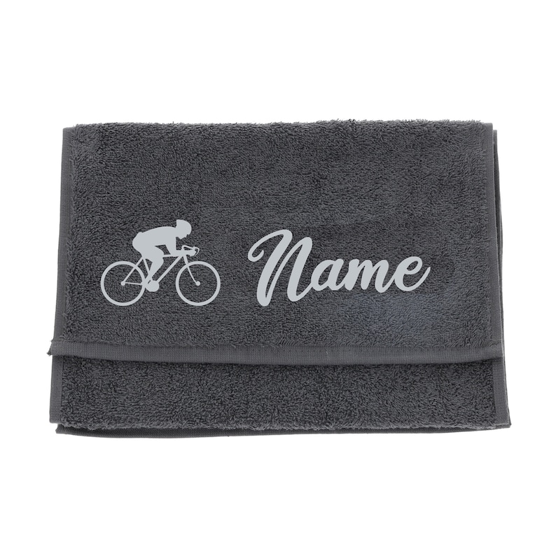 Puede incluir: Toalla de algod&oacute;n gris con una silueta blanca de un ciclista en bicicleta y la palabra "Name" bordada en blanco.