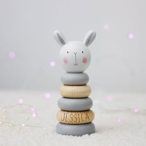 May include: A grey and white wooden stacking toy shaped like a bunny with the name "Jessica" engraved on one of the rings.