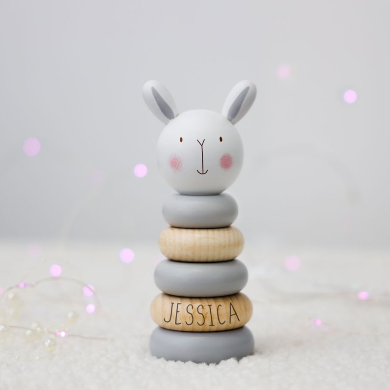 May include: A grey and white wooden stacking toy shaped like a bunny with the name "Jessica" engraved on one of the rings.