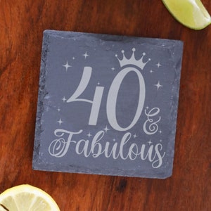May include: A black slate coaster with the text "40 & Fabulous" in silver lettering. A crown is above the number 40 and there are small stars around the text.