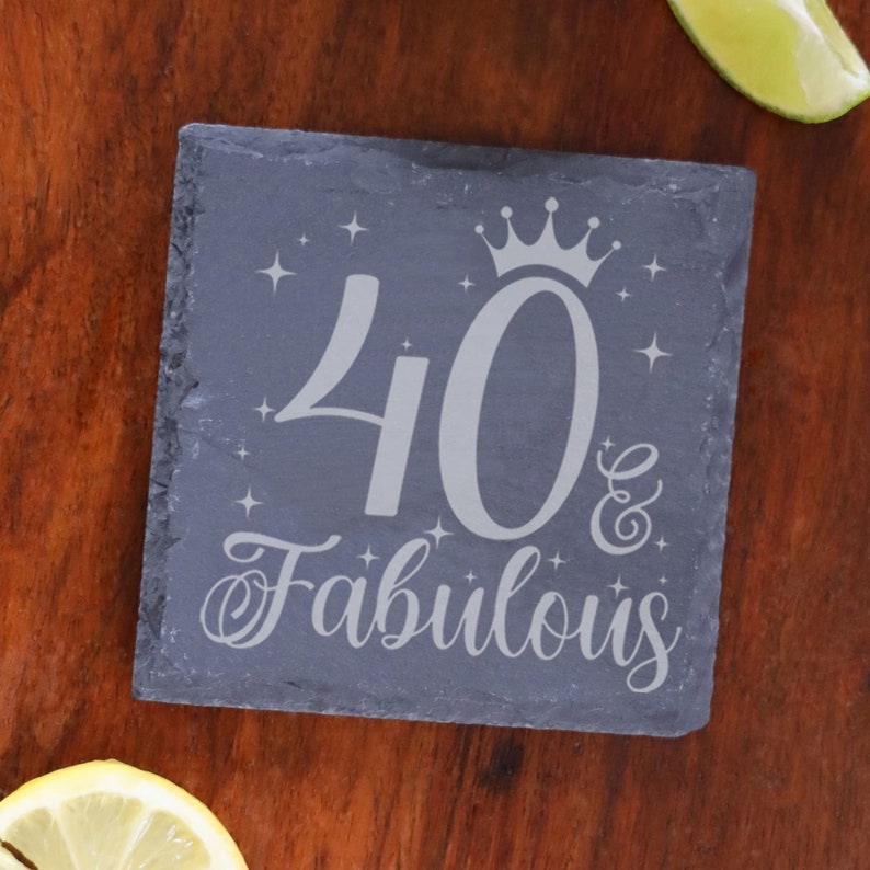 May include: A black slate coaster with the text "40 & Fabulous" in silver lettering. A crown is above the number 40 and there are small stars around the text.