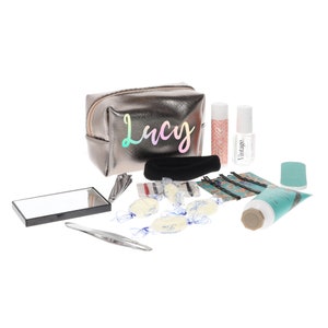 May include: A silver metallic makeup bag with the name "Lucy" printed on it. The bag is open and contains various items, including a small mirror, a pair of tweezers, a hair scrunchie, hair clips, and several small white and blue packages.