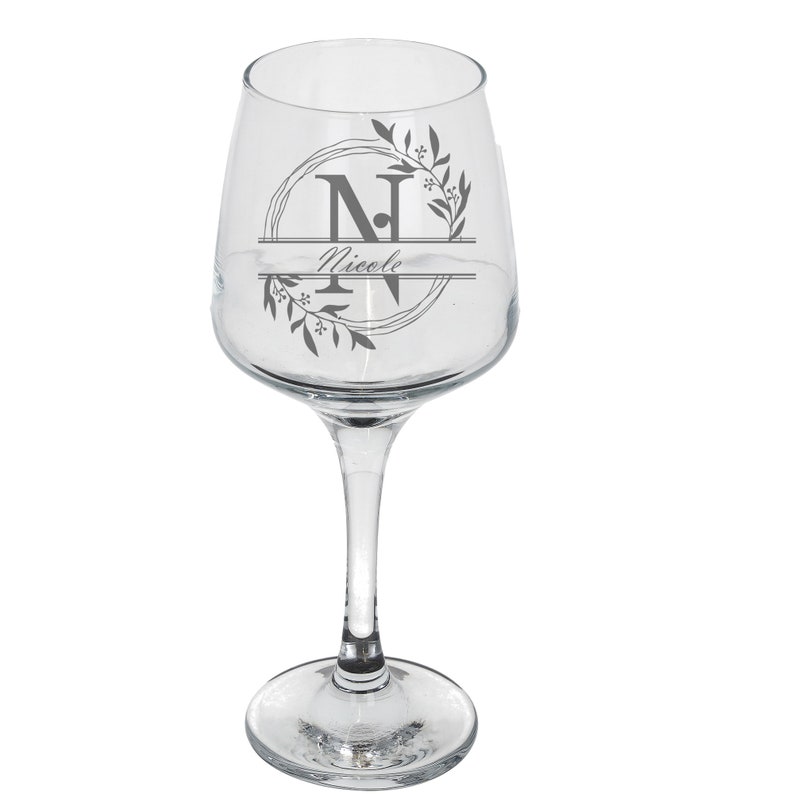 Puede incluir: Una copa de vino de vidrio transparente con un dise&ntilde;o en blanco y negro que presenta una corona floral con la letra "N" y el nombre "Nicole" en una fuente de escritura.