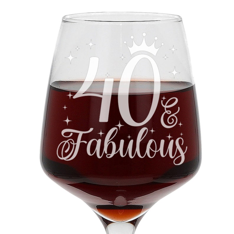 May include: A clear glass wine glass with a white design that says "40 & Fabulous" with a crown above the 40. The glass is filled with red wine.