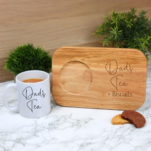 May include: A white mug with "Dad's Tea" in black script sits next to a wooden tea and biscuit board. The board has a circular indentation for the mug and the words "Dad's Tea + Biscuits" are etched into the wood. Two biscuits are on the marble surface.
