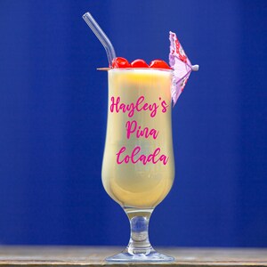 Puede incluir: Un vaso de c&oacute;ctel de pi&ntilde;a con una sombrilla de papel rosa y cerezas marrasquino. La bebida est&aacute; etiquetada como "Hayley's Pina Colada".