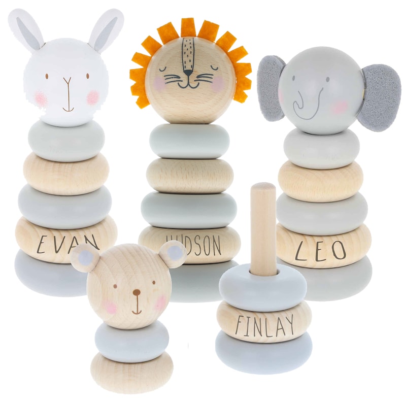 May include: Set of five wooden stacking rings with animal faces. The rings are painted in light blue and natural wood tones. Each ring has a name on it: Evan, Hudson, Leo, Finlay.