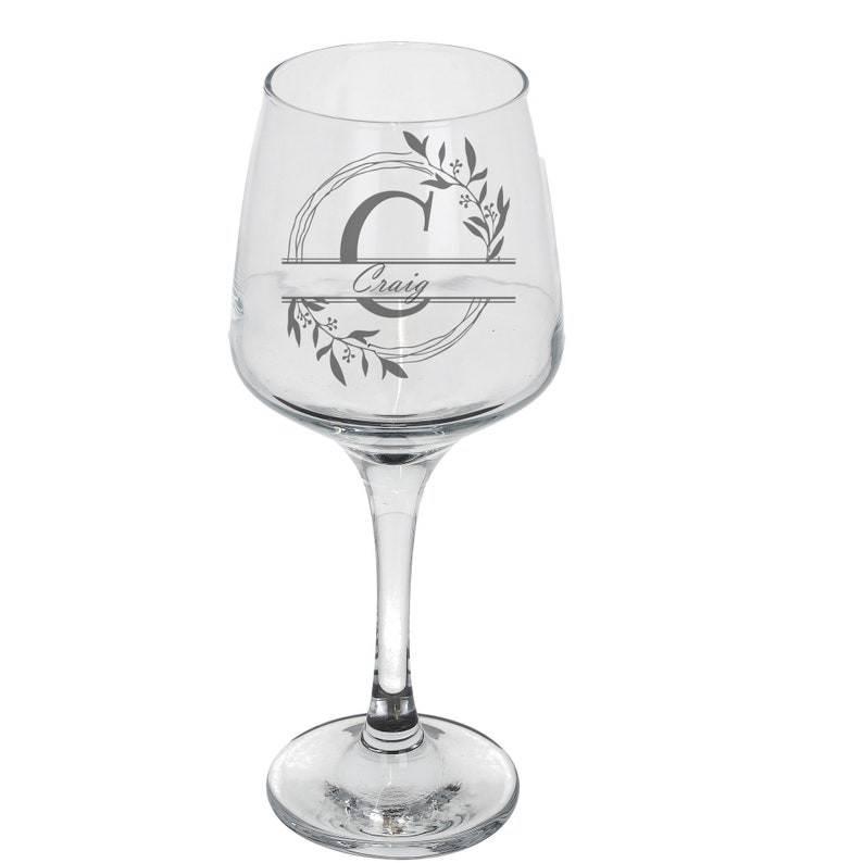 Puede incluir: Una copa de vino de vidrio transparente con un dise&ntilde;o en blanco y negro que presenta una corona de flores y la letra "C" con el nombre "Craig" impreso debajo.