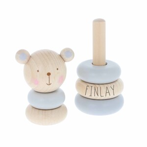 May include: A wooden stacking toy with a bear face on the bottom piece and three rings with the name "FINLAY" on one of the rings. The rings are light blue and the bear is natural wood.