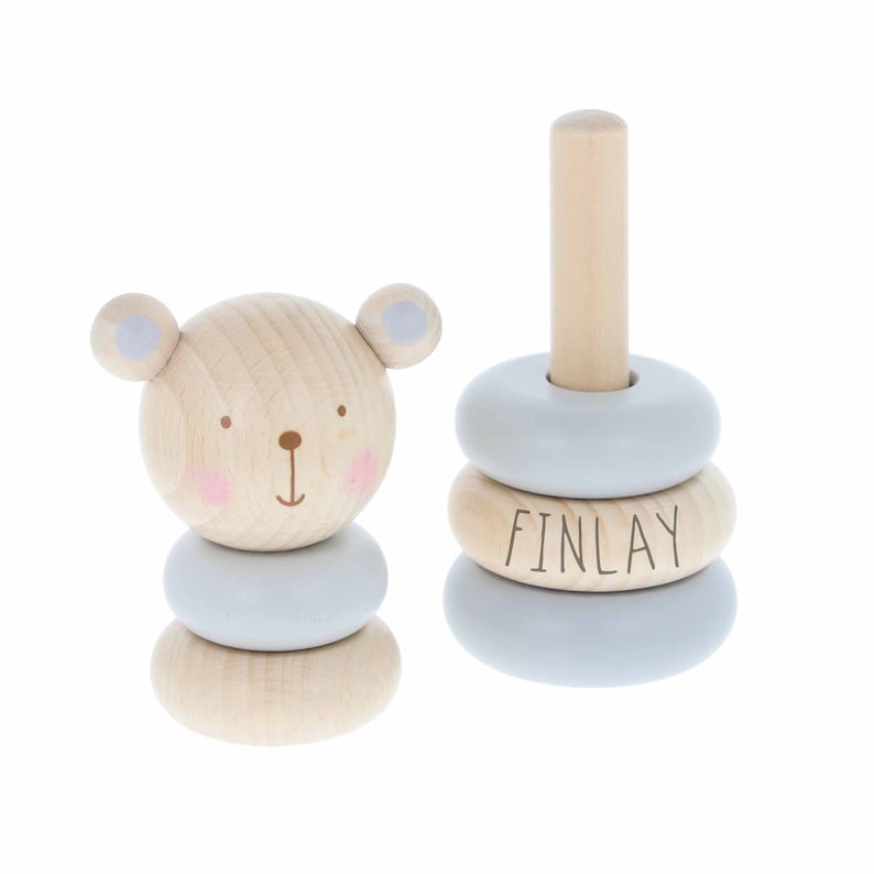 May include: A wooden stacking toy with a bear face on the bottom piece and three rings with the name "FINLAY" on one of the rings. The rings are light blue and the bear is natural wood.