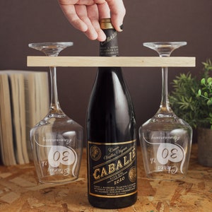 May include: Two wine glasses with the text "30th Anniversary" etched on them, a bottle of red wine with the label "Cuv&eacute;e Vieilles Vignes CABALIE PAYS DOC 2010" and a wooden wine rack.