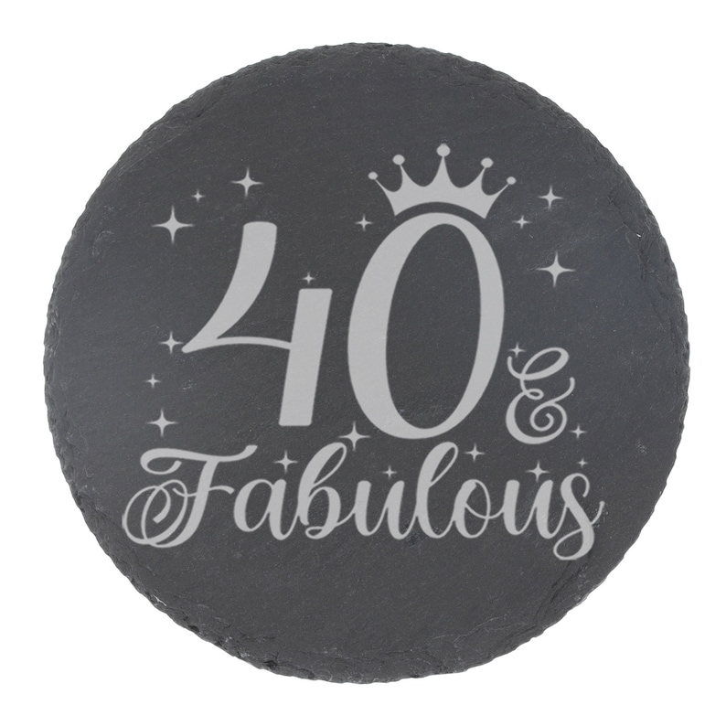 May include: A black slate round coaster with a silver inscription that reads "40 & Fabulous" with a crown above the number 40.