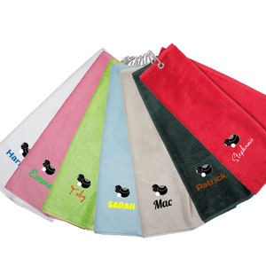 May include: A selection of colourful microfiber golf towels, each with a name printed in a different colour. The towels are attached to a metal ring. Each towel has a black and white design.