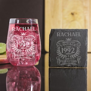 Puede incluir: Una copa de vino sin tallo personalizada y un posavasos de pizarra con el nombre "Rachael" y el texto "Premium Quality Vintage 1992 Limited Edition Aged to Perfection".