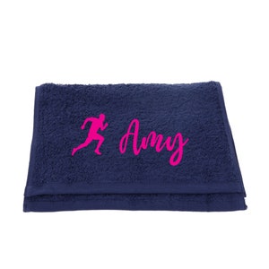 Puede incluir: Una toalla azul marino con una figura de corredor rosa y el nombre "Amy" bordado.