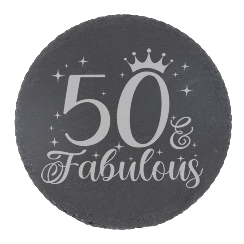 May include: A black slate round coaster with a silver inscription that reads "50 & Fabulous" with a crown above the number 50.