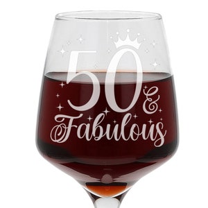 May include: A clear glass wine glass with a white etched design that says "50 & Fabulous" with a crown above the number 50.