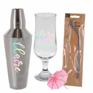 Puede incluir: Un set de c&oacute;cteles con una coctelera plateada, un vaso con la inscripci&oacute;n "Me encanta la Pi&ntilde;a Colada", una sombrilla de papel rosa y una pajita de acero inoxidable reutilizable con un cepillo de limpieza.