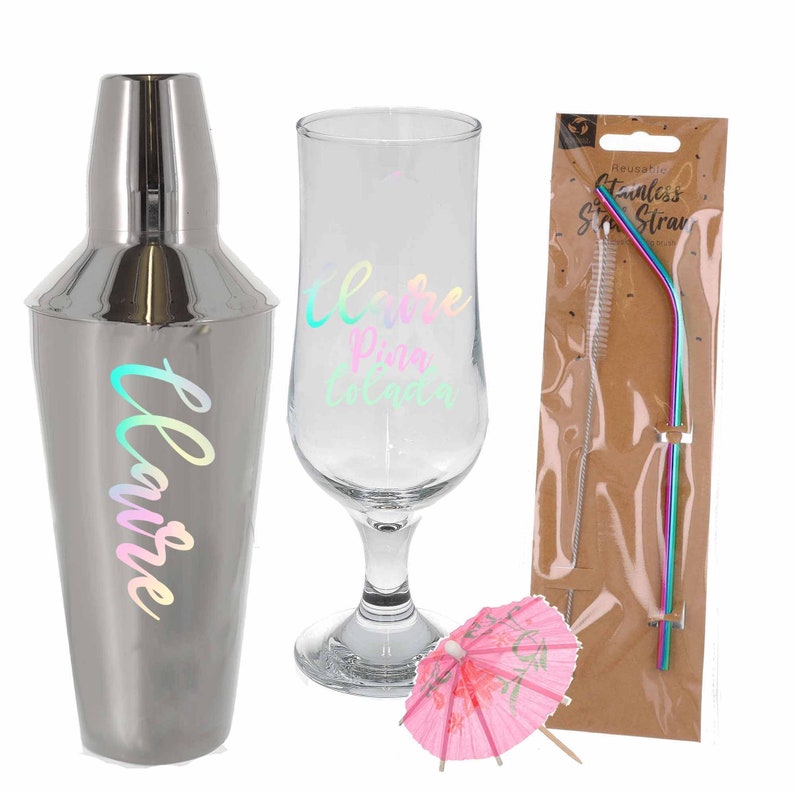 Puede incluir: Un set de c&oacute;cteles con una coctelera plateada, un vaso con la inscripci&oacute;n "Me encanta la Pi&ntilde;a Colada", una sombrilla de papel rosa y una pajita de acero inoxidable reutilizable con un cepillo de limpieza.