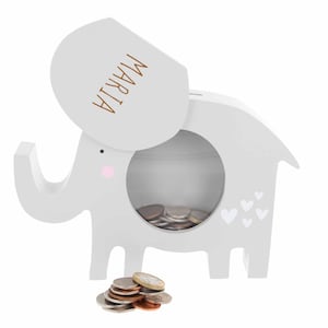 May include: Grey wooden elephant money box with a slot on the side and a removable lid. The lid has the name "MARIJA" written on it. The elephant has pink cheeks and white hearts on its side. There are coins in the money box and on the floor.