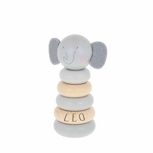 May include: A grey and natural wood stacking toy shaped like an elephant with the name "LEO" on one of the rings.