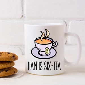 May include: White ceramic mug featuring a cartoon illustration of a teacup with steam, a teabag, and the text "Liam is Six-Tea".