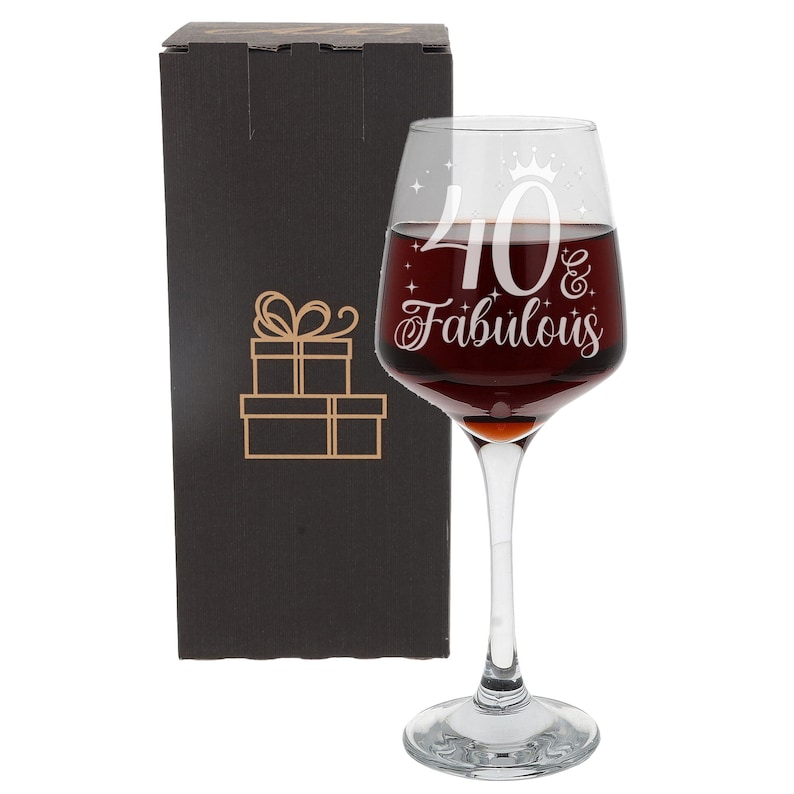 May include: A clear glass wine glass with a stem and a wide bowl. The glass is etched with the text "40 & Fabulous" and a small crown. The glass is in a black gift box.