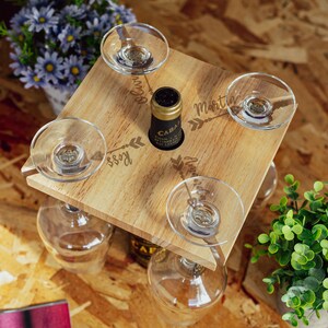 May include: Wooden wine rack with four glass holders and a bottle holder. The rack is engraved with the names "Olivia", "Ross", "Martin", and "Amanda" and arrows pointing to each name.