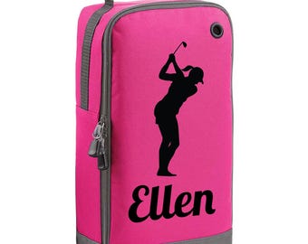 May include: A hot pink golf shoe bag with a black silhouette of a golfer swinging a club. The bag has a gray zipper, handle, and trim. The name "Ellen" is printed in black script on the front.