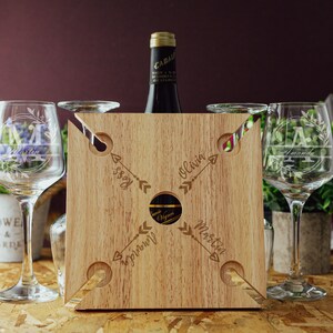 May include: Wooden wine carrier with four slots for glasses and a center slot for a bottle. The carrier is engraved with the names "Olivia", "Martin", "Issy", and "Aprilyn" and arrows pointing to each name.