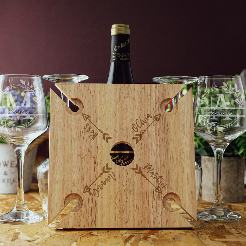 May include: Wooden wine carrier with four slots for glasses and a center slot for a bottle. The carrier is engraved with the names "Olivia", "Martin", "Issy", and "Aprilyn" and arrows pointing to each name.