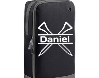 May include: Black golf shoe bag with a gray trim and handle. The bag features a white graphic of crossed golf tees and the name "Daniel" in white. The bag has a zippered closure and a small side pocket.