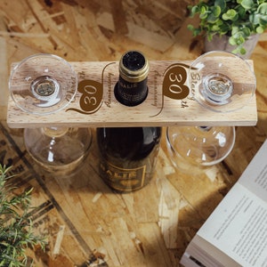 May include: Wooden wine bottle holder with two glass holders. The holder is engraved with the text "30th Anniversary" and two hearts. The bottle holder is a great gift for a couple celebrating their 30th anniversary.