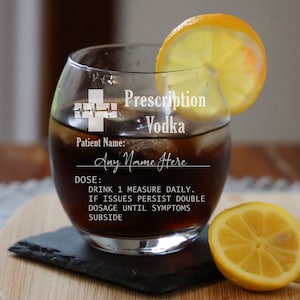 May include: A clear glass with a humorous prescription vodka label. The label includes a medical cross, a heartbeat line, and the text "Prescription Vodka". The glass is filled with a dark liquid and a lemon wedge is on the rim. The text on the label reads "Patient Name: Any Name Here Dose: Drink 1 measure daily. If issues persist double dosage until symptoms subside."