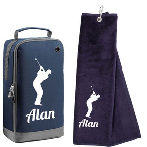 May include: A navy blue golf shoe bag and a matching golf towel. Both items feature a white silhouette of a golfer and the name "Alan". The shoe bag has a handle and a zipper. The towel has a metal clip.
