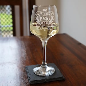 May include: A clear glass wine glass filled with a light-colored liquid, featuring an etched design that reads Premium Quality Vintage Limited 1946 Edition Aged to Perfection, complete with a crown and laurel wreath graphic on the front surface.