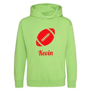 Könnte beinhalten: Hellgrüner Kapuzenpullover mit rotem Football-Motiv und dem Namen "Kevin" in roter Schrift. Der Pullover hat eine Vordertasche und eine Kapuze mit Kordelzug. Das Football-Motiv befindet sich in der Mitte.