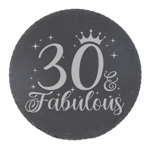 May include: A black slate round coaster with a silver inscription that reads "30 & Fabulous" with a crown above the number 30.