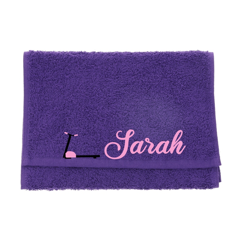 Puede incluir: Toalla morada con un gr&aacute;fico rosa de una cinta de correr y el nombre "Sarah" bordado en rosa.