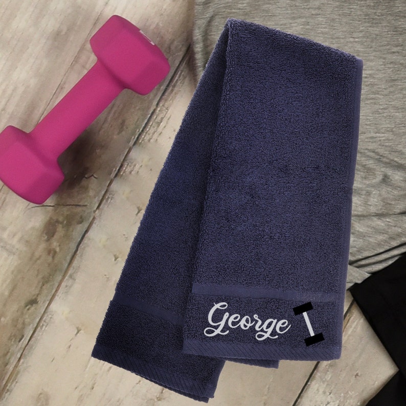 Puede incluir: Una toalla de gimnasio azul oscuro con el nombre "George" y un s&iacute;mbolo de mancuerna bordado.
